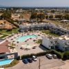 Aerial view of a seaside resort with white apartments, a central pool area, and sun loungers around the pool.