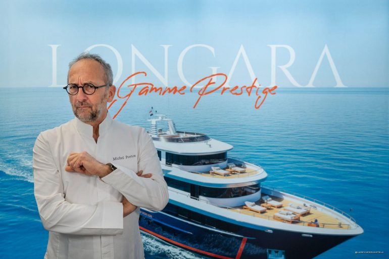 Chef Michel Portos in a white coat with folded arms stands before a blue backdrop featuring a luxury yacht and the text ‘Gamme Prestige’.