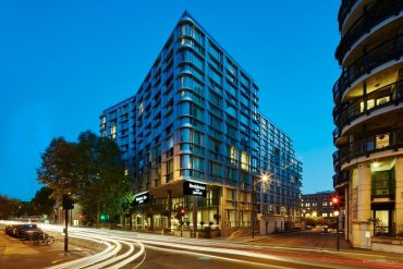 Corner of a modern glass hotel building at dusk with light-trail traffic on the street corner