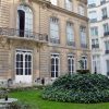 Historic hotel courtyard with a circular ivy-covered fountain statue and wrought-iron tables and chairs on a green lawn.