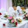 Wedding reception table set with pink and red floral centerpieces, glassware, and white linens.
