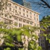 Facade of the Hotel Principe di Savoia with arched windows, framed by green tree branches and a blue sky above.