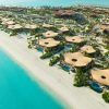 Aerial view of a beachside resort with many circular beige canopy structures along a white-sand shore and turquoise water nearby.