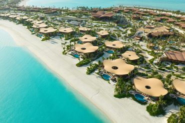 Aerial view of a beachside resort with many circular beige canopy structures along a white-sand shore and turquoise water nearby.