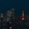 Night city skyline with illuminated skyscrapers and a tall orange-lit tower.