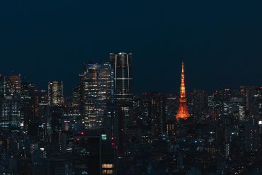 Night city skyline with illuminated skyscrapers and a tall orange-lit tower.