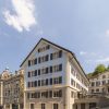 Blue and beige hotel building with black shutters, labeled Villa Florhof, on a cobblestone street against a clear blue sky.