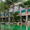 Resort courtyard with a turquoise pool, palm trees, hammocks, and a stone-clad building facade.