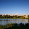 Wide lake scene with a grassy bank, a line of trees, and a stone castle on the far shore under a clear blue sky.