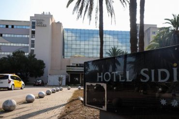 Hotel Sidi exterior with palm trees, glass façade, and a foreground sign reading HOTEL SIDI