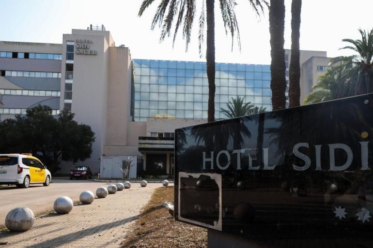Hotel Sidi exterior with palm trees, glass façade, and a foreground sign reading HOTEL SIDI