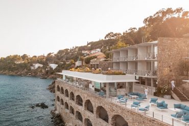 Resort terrace built into a rocky shoreline overlooking the sea with blue couches and white chairs.