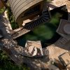 Aerial view of a curved wooden deck surrounding a circular pool, with lounge chairs and greenery.