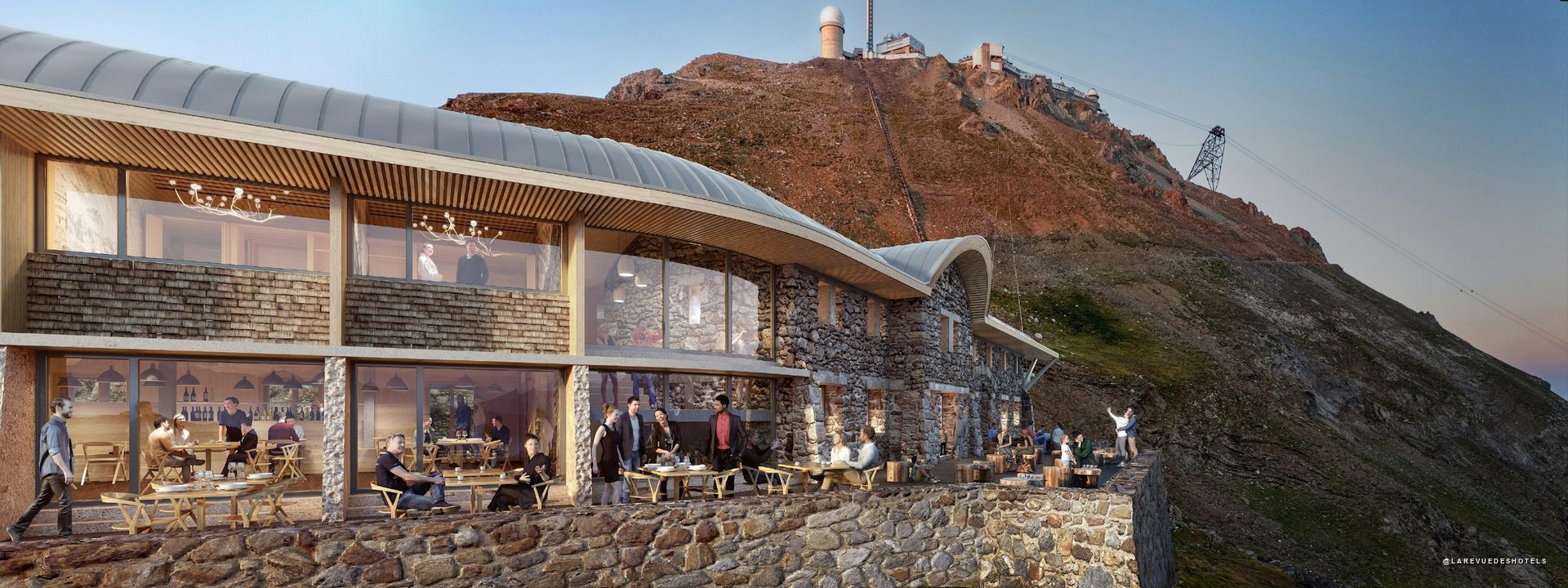 Stone hotel built into a mountain with a glass-walled dining area and outdoor terrace filled with guests.