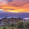 Luxurious resort hotel perched on hills with a sunset over a lake and purple mountains in the distance.