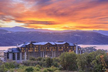 Luxurious resort hotel perched on hills with a sunset over a lake and purple mountains in the distance.