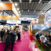 Busy exhibition hall with orange Selectour banners, pink carpet, and attendees visiting travel booths.