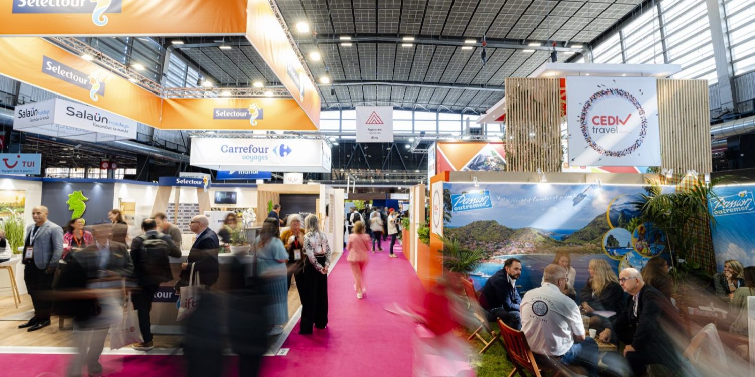Busy exhibition hall with orange Selectour banners, pink carpet, and attendees visiting travel booths.