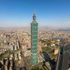 Aerial view of Taipei with the tall Taipei 101 skyscraper at the center and dense city blocks around.