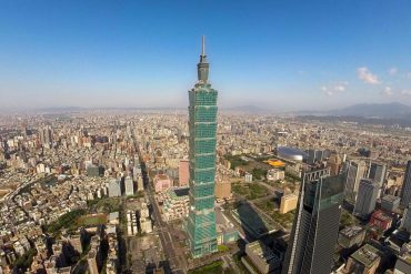 Aerial view of Taipei with the tall Taipei 101 skyscraper at the center and dense city blocks around.