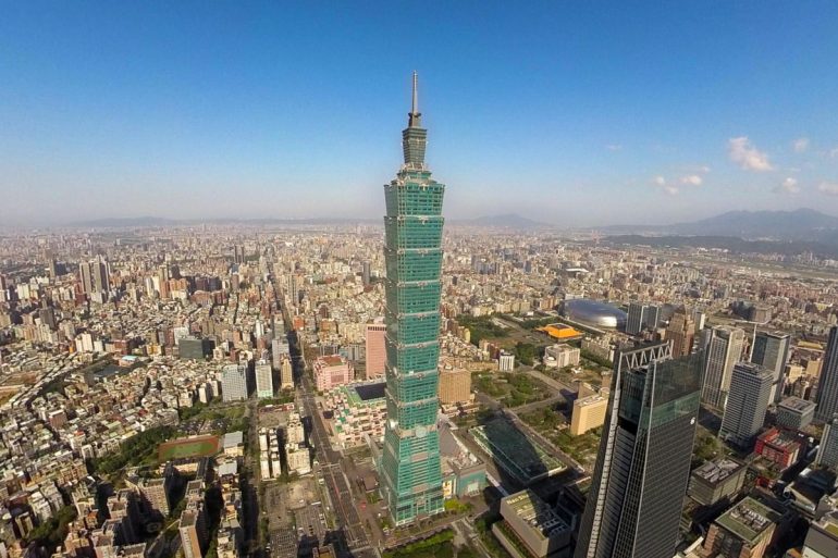 Aerial view of Taipei with the tall Taipei 101 skyscraper at the center and dense city blocks around.