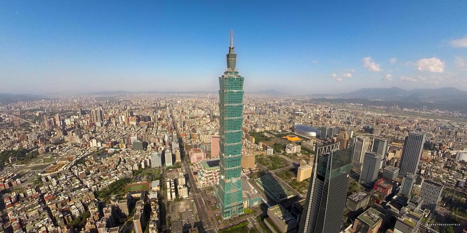 Aerial view of Taipei with the tall Taipei 101 skyscraper at the center and dense city blocks around.
