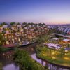 Resort complex at dusk with terraced buildings along a winding canal, palm trees and warm lights glowing at the terraces.