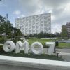 Large white 3D letters spell 'OMO7' in a landscaped plaza with a modern, irregular-patterned white building behind it.