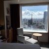 Hotel room with a large window offering a city view, a gray armchair and small round table by the window.
