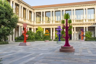 Historic courtyard with a two-story colonnade and bright abstract tree sculptures in red, purple, and orange.