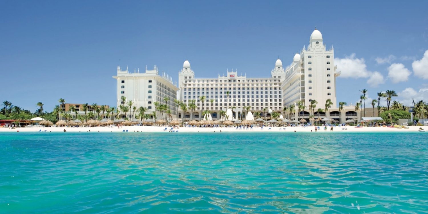 White hotel resort on a sandy beach with palm trees and turquoise sea.