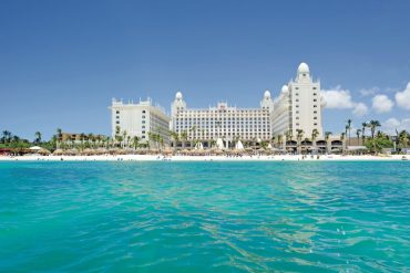 White hotel resort on a sandy beach with palm trees and turquoise sea.