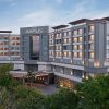 Exterior view of The Aarlis hotel: a modern, multi-wing building with warm-lit windows at dusk, surrounded by trees