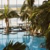 Indoor tropical pool area with palm trees, glass walls, and stepping platforms.