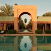 Piscine principale de l'Amanjena a Marrakech, arche mauresque rose et allee de palmiers au coucher du soleil