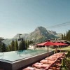 Le bassin extérieur à débordement du Burg Hotel Oberlech, transats rouges et télécabine de Lech-Oberlech devant le sommet de l'Omeshorn