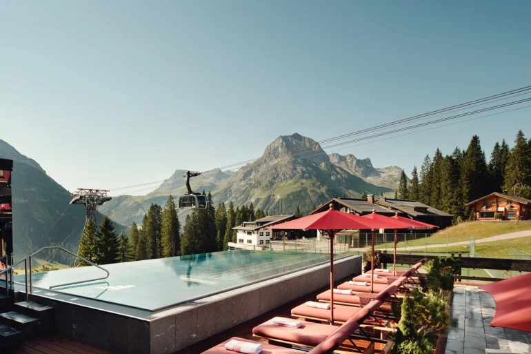 Le bassin extérieur à débordement du Burg Hotel Oberlech, transats rouges et télécabine de Lech-Oberlech devant le sommet de l'Omeshorn