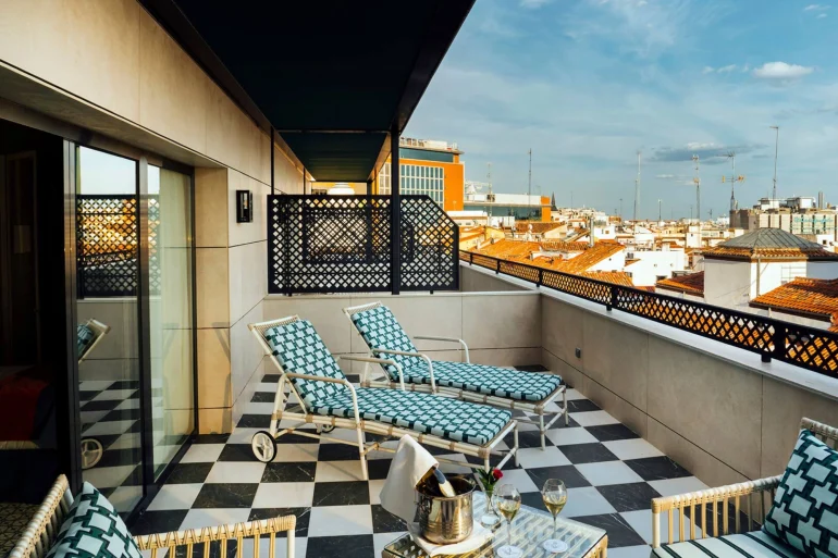 Terrasse d'une chambre de Casa Verbena Madrid, transats en rotin et sol en damier noir et blanc au-dessus des toits de tuiles de Madrid