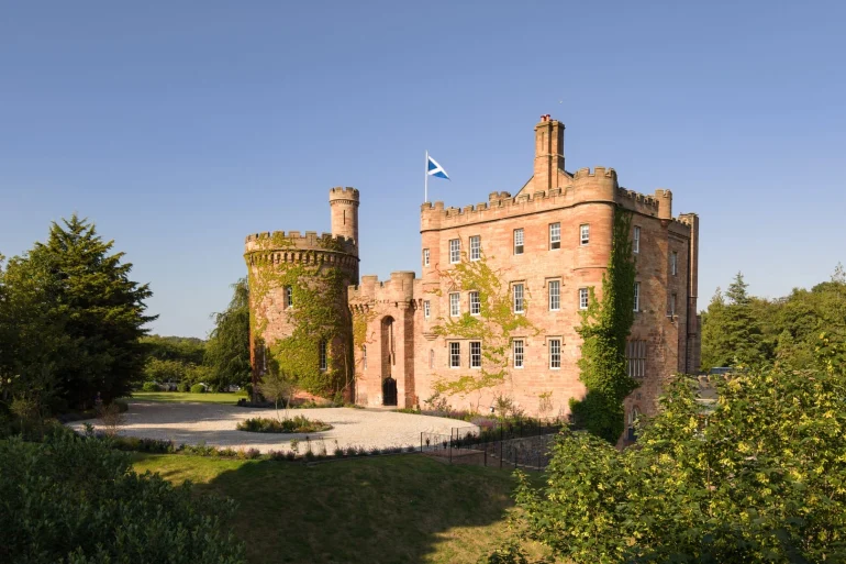 Façade en grès rouge du Dalhousie Castle, château-hôtel près d'Édimbourg, avec sa tour ronde et le drapeau écossais