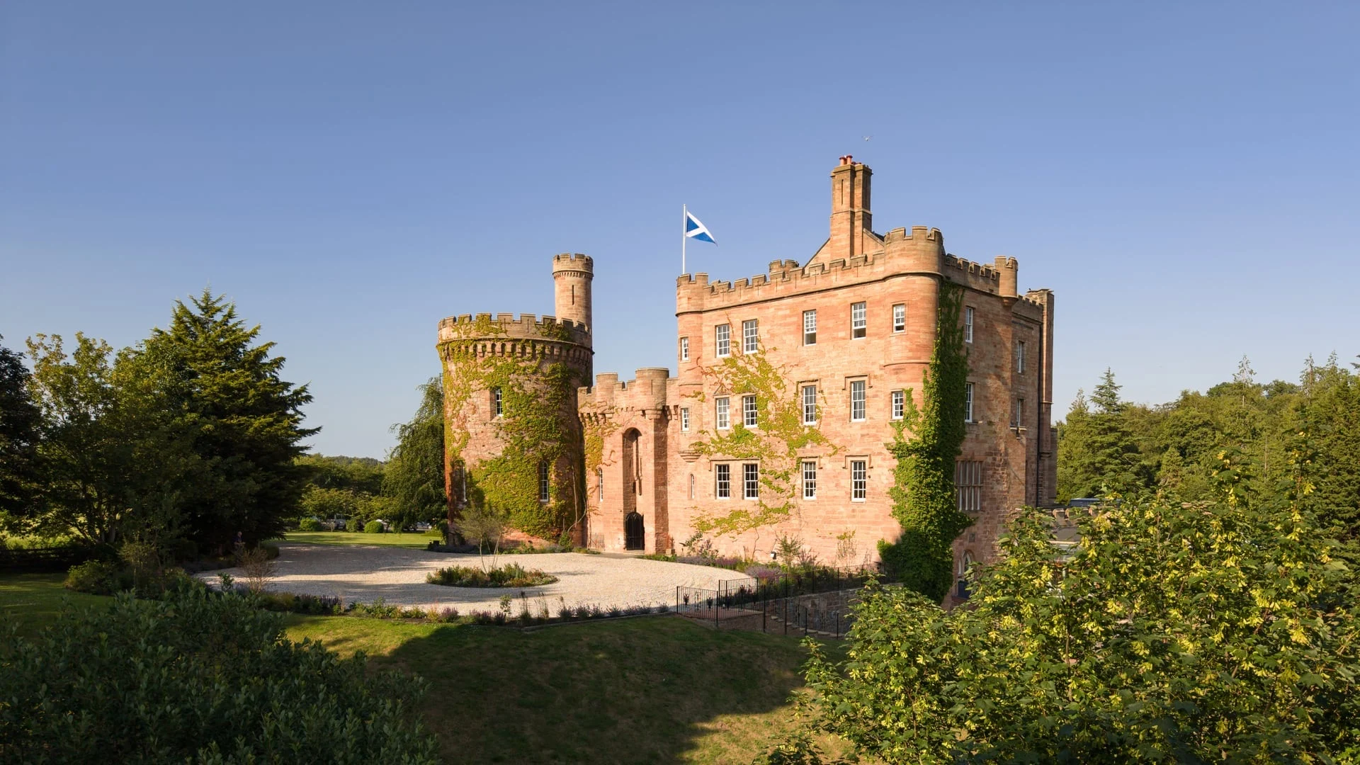 Façade en grès rouge du Dalhousie Castle, château-hôtel près d'Édimbourg, avec sa tour ronde et le drapeau écossais