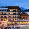 Façade éclairée du Grand Hôtel de Valloire et du Galibier un soir d'hiver, toits enneigés et sommets de la vallée de la Maurienne en arrière-plan