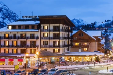 Façade éclairée du Grand Hôtel de Valloire et du Galibier un soir d'hiver, toits enneigés et sommets de la vallée de la Maurienne en arrière-plan
