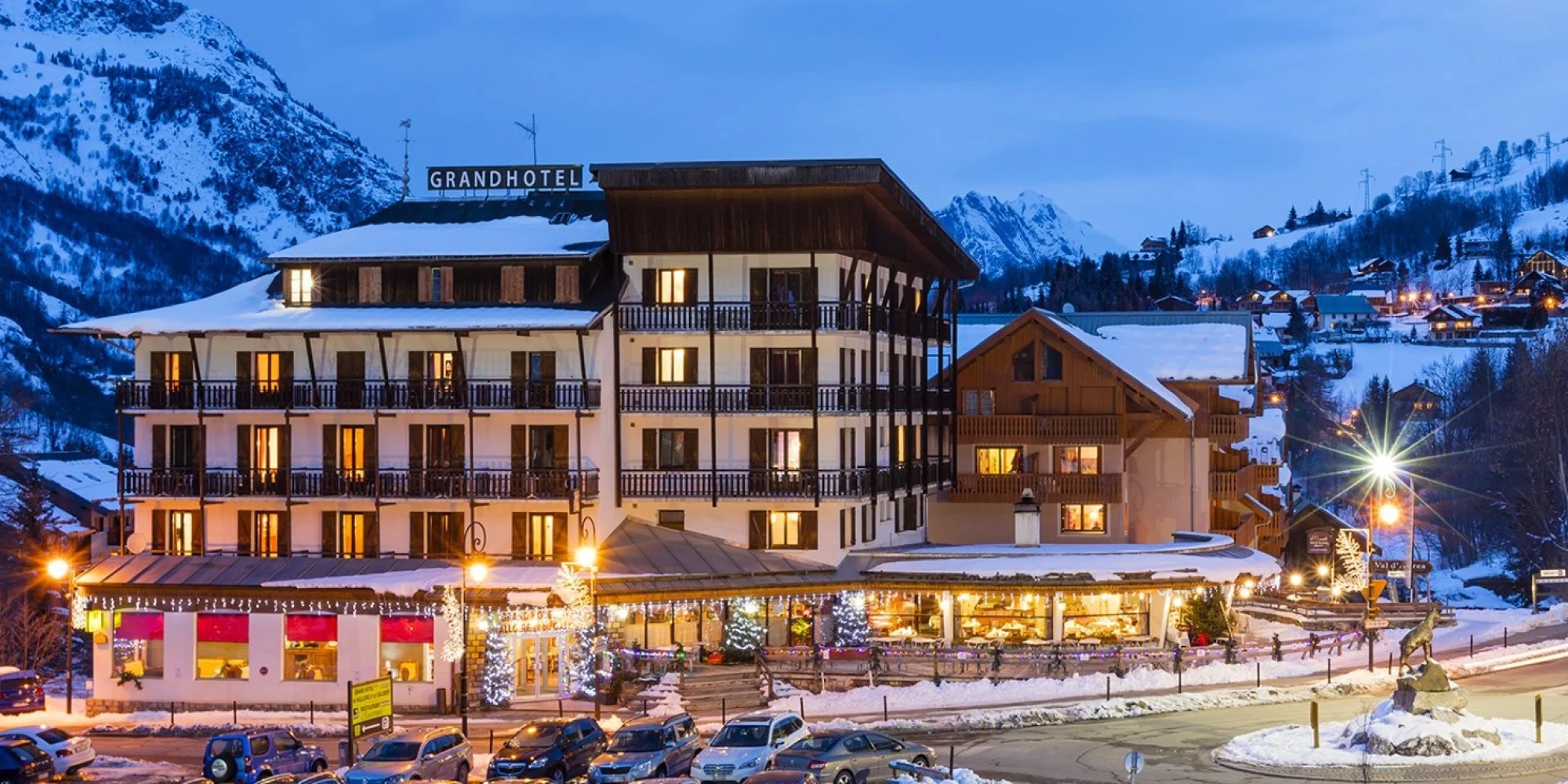 Façade éclairée du Grand Hôtel de Valloire et du Galibier un soir d'hiver, toits enneigés et sommets de la vallée de la Maurienne en arrière-plan