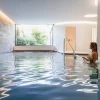 La piscine intérieure de 17 mètres du spa des Haras Hôtel, à Strasbourg, éclairée par une baie vitrée ouverte sur la végétation