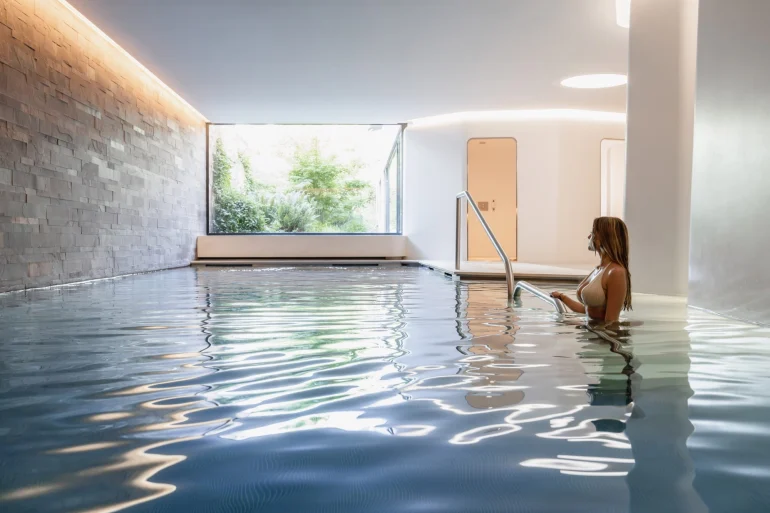 La piscine intérieure de 17 mètres du spa des Haras Hôtel, à Strasbourg, éclairée par une baie vitrée ouverte sur la végétation