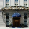 Entrée principale de l'hôtel : marquise en fer forgé doré, auvent bleu, deux portiers en livrée