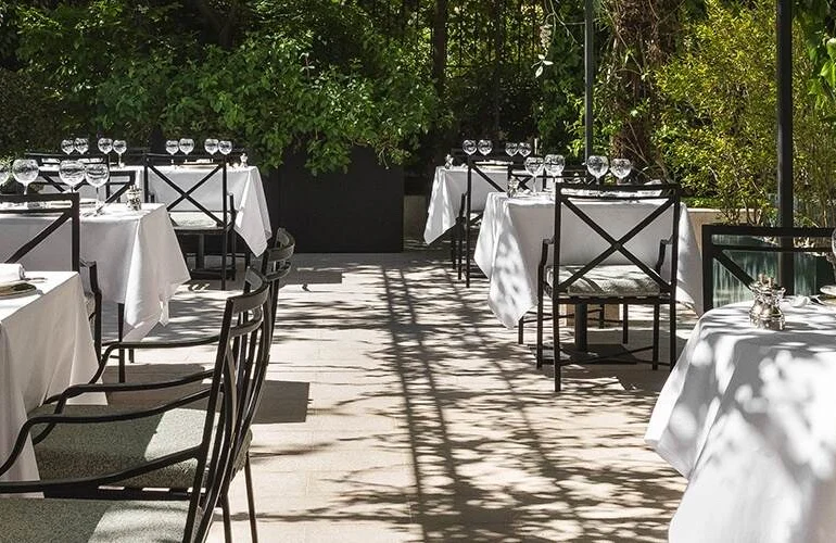 Tables nappées de blanc de Maison Roland, le bistrot du jardin du Shangri-La Paris, sous les arbres de l'avenue d'Iéna