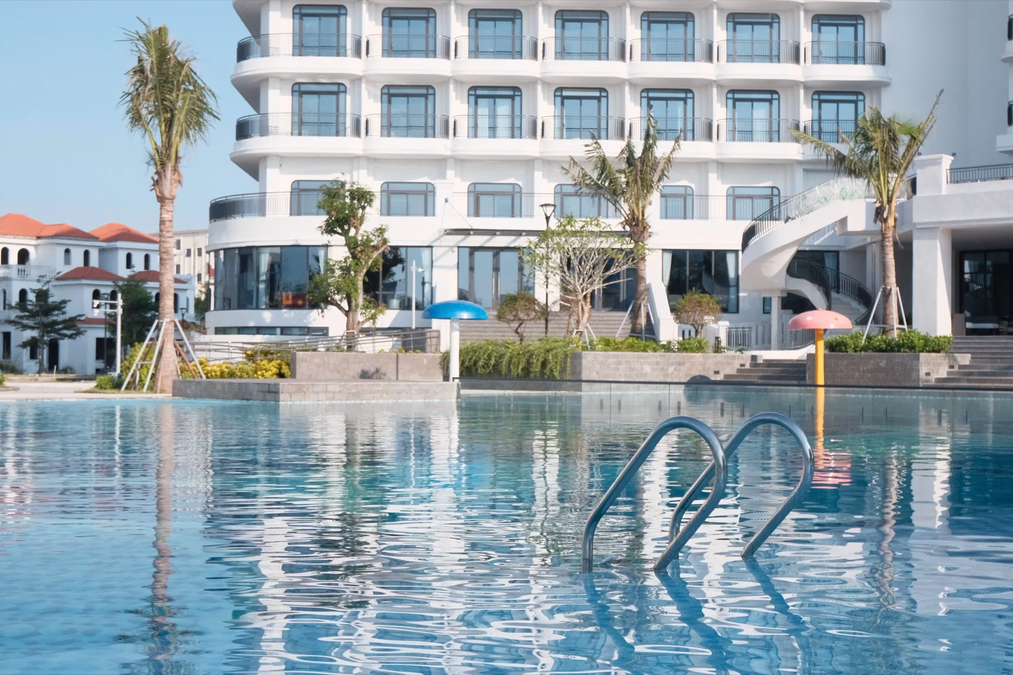 Facade blanche du Tra Co Long Beach Hotel & Resort a Mong Cai vue depuis la grande piscine exterieure bordee de palmiers