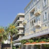 Façade en pierre de la Villa Argentina à Dubrovnik, balcons à balustres et baies en arc, aile moderne de l'hôtel en retrait derrière les palmiers