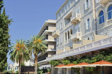Façade en pierre de la Villa Argentina à Dubrovnik, balcons à balustres et baies en arc, aile moderne de l'hôtel en retrait derrière les palmiers